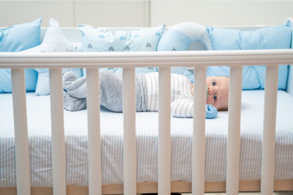A baby with pacifier in mouth is lying in the crib